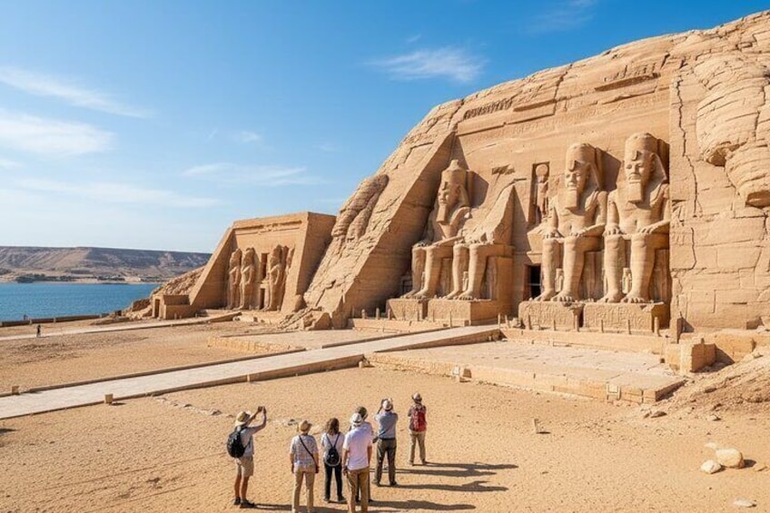 A large ancient Egyptian temple with a clear view of the pharaoh's statues and a group of tourists taking photos. 1