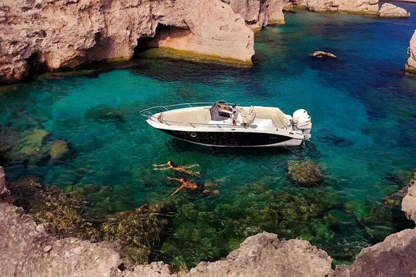 A boat anchored in a clear blue sea with rocky cliffs in the background. 1