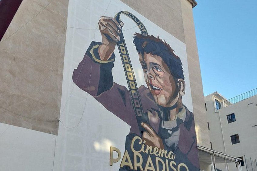 Une fresque représentant une personne tenant un appareil de cinéma, avec les mots « Cinema Paradiso » inscrits sur un bâtiment. 2