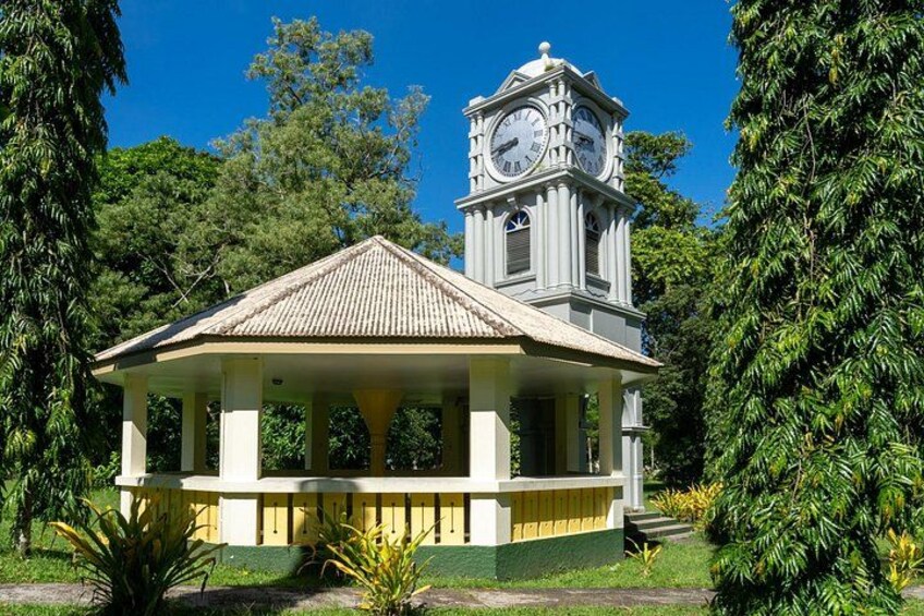 Een kiosk met een klokkentoren, omgeven door weelderige begroeiing. 2