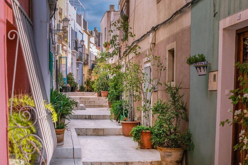 A narrow alley with steps leading up to a building, surrounded by colorful buildings and potted plants. 4
