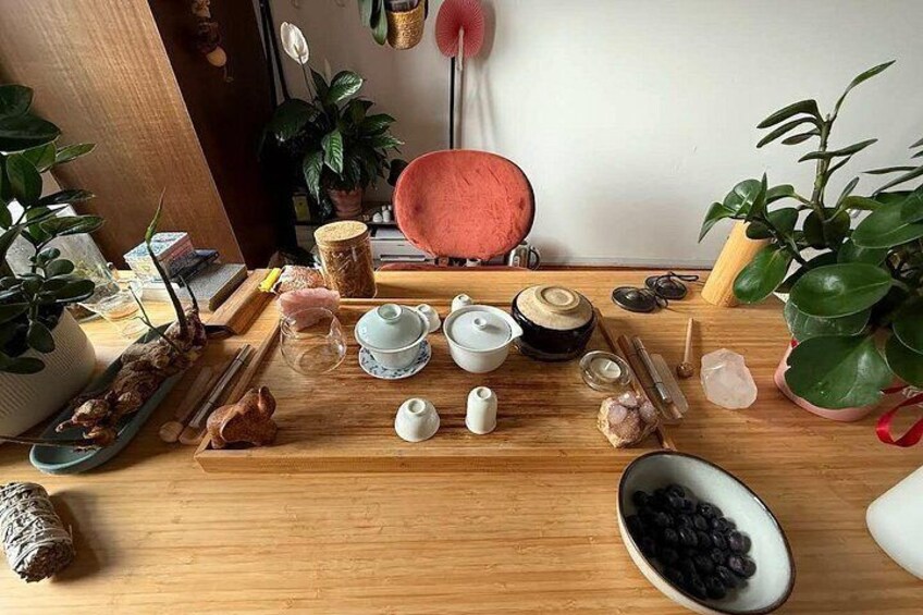 A wooden table with various tea utensils, a pink bowl, and green plants. 5