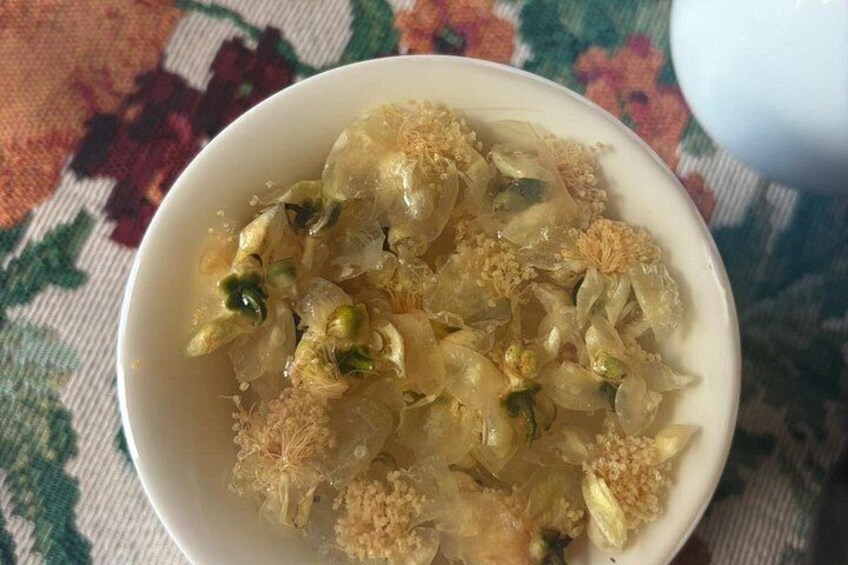 A bowl of food with translucent ingredients and green elements, possibly nuts, on a patterned tablecloth. 3