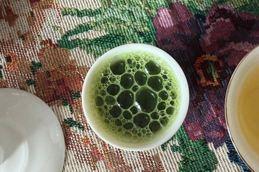 A cup of green tea with bubbles on a tablecloth. 2