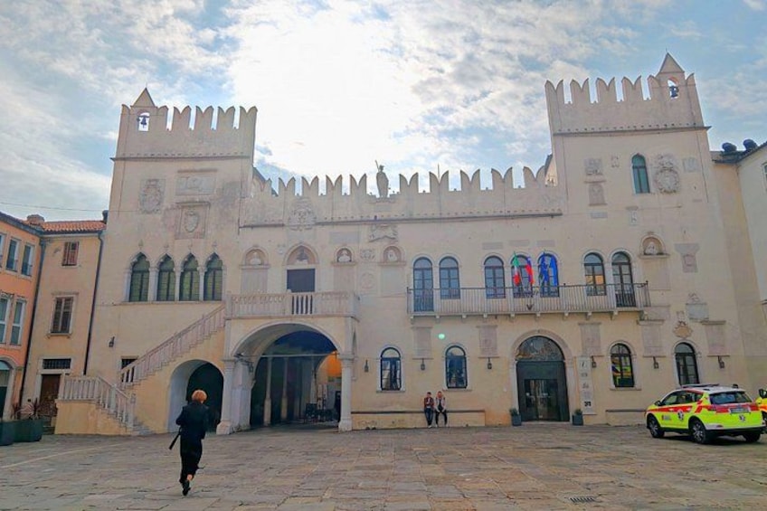 A historic building with a central archway, two towers with crenellations, and a paved courtyard. 3