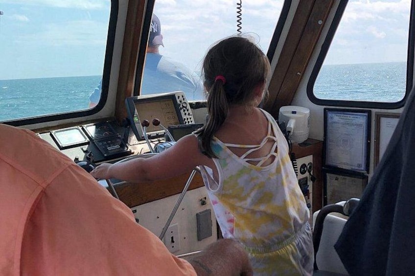 A child operating a boat's controls, with a person in the background and a view of the sea. 5