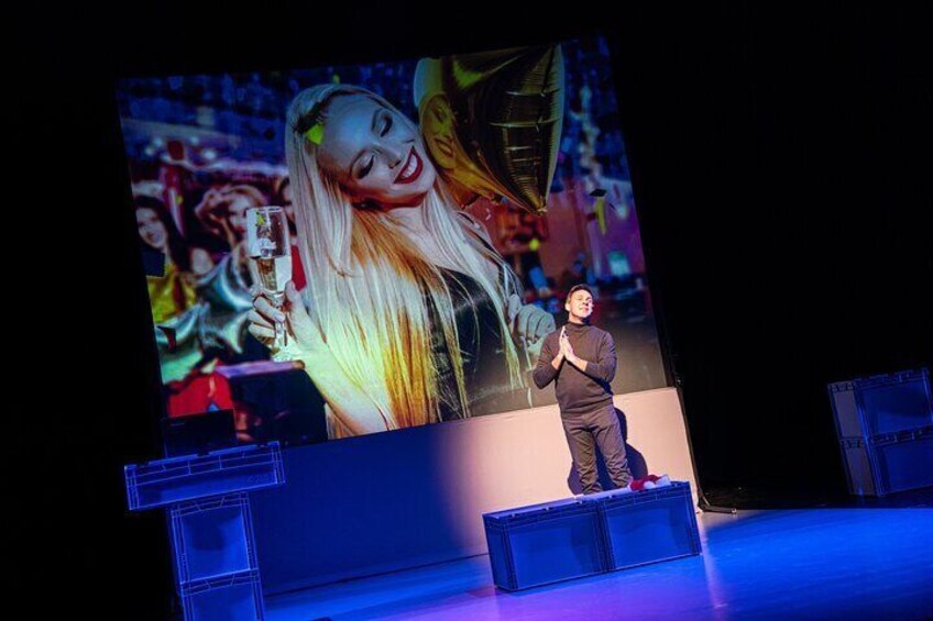 Una persona en el escenario frente a una pantalla grande que muestra a un artista de fondo. 3