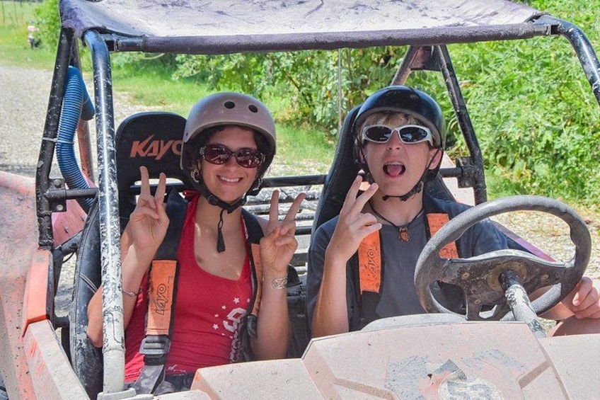 Two people in a vehicle with a steering wheel, wearing helmets and a red tank top. 1