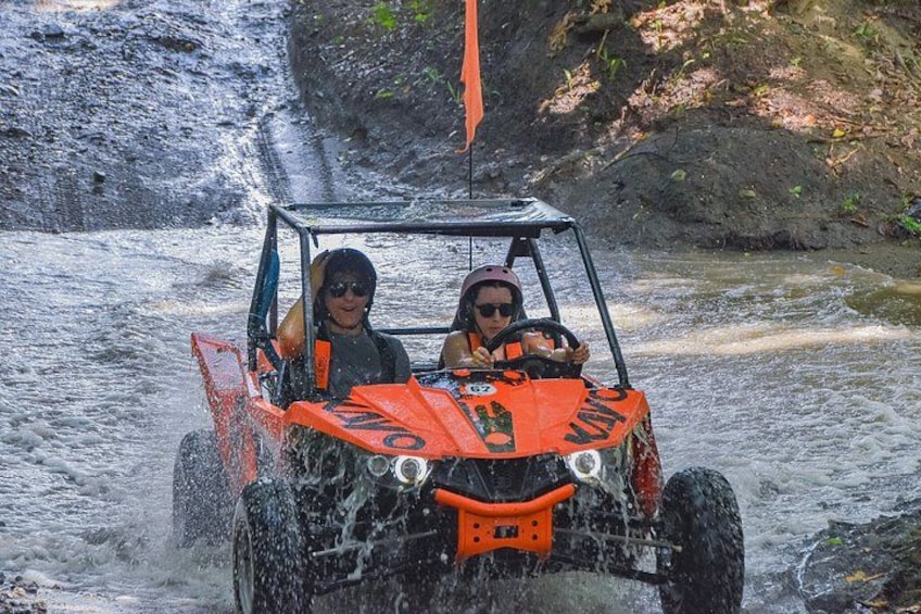 A vehicle driving through a water body with a rocky landscape in the background. 2