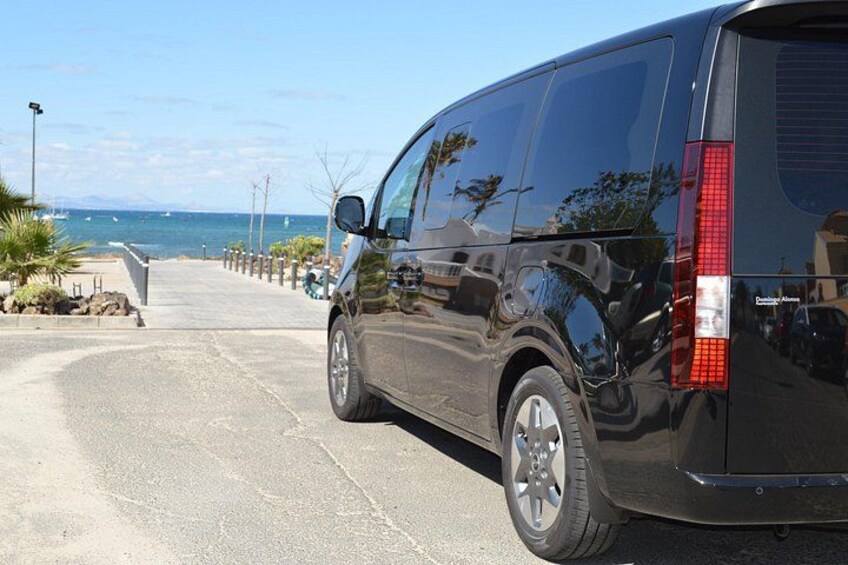 A black van parked on a coastal road with a clear view of the ocean and a paved walkway. 2