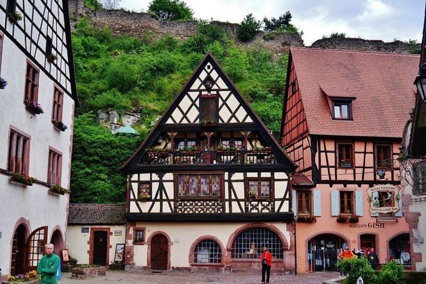 Un edificio tradicional con entramado de madera y un balcón, rodeado de otros edificios históricos y una ladera. 4