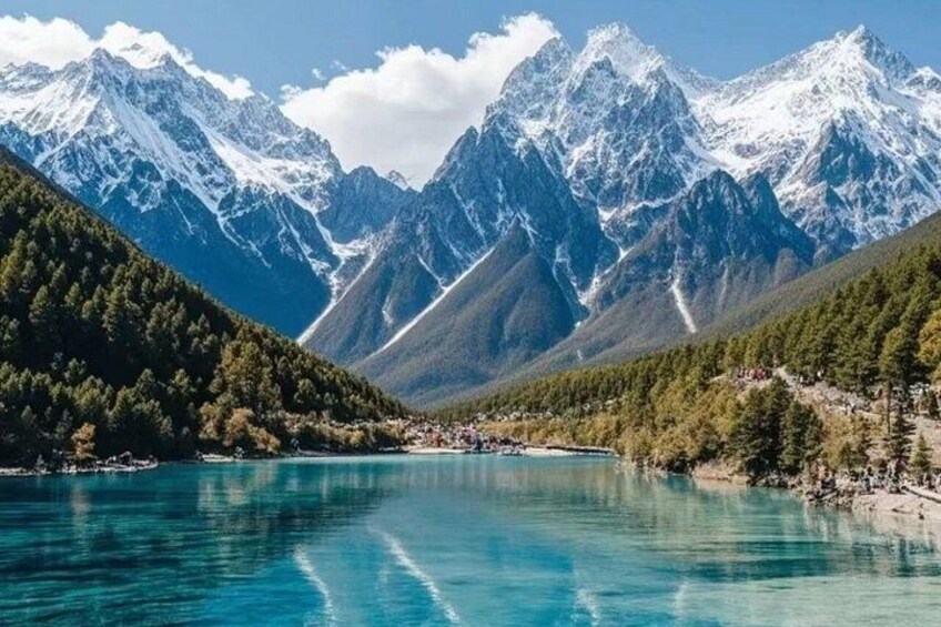 A lake surrounded by mountains, clear blue water, and dense forest. 5