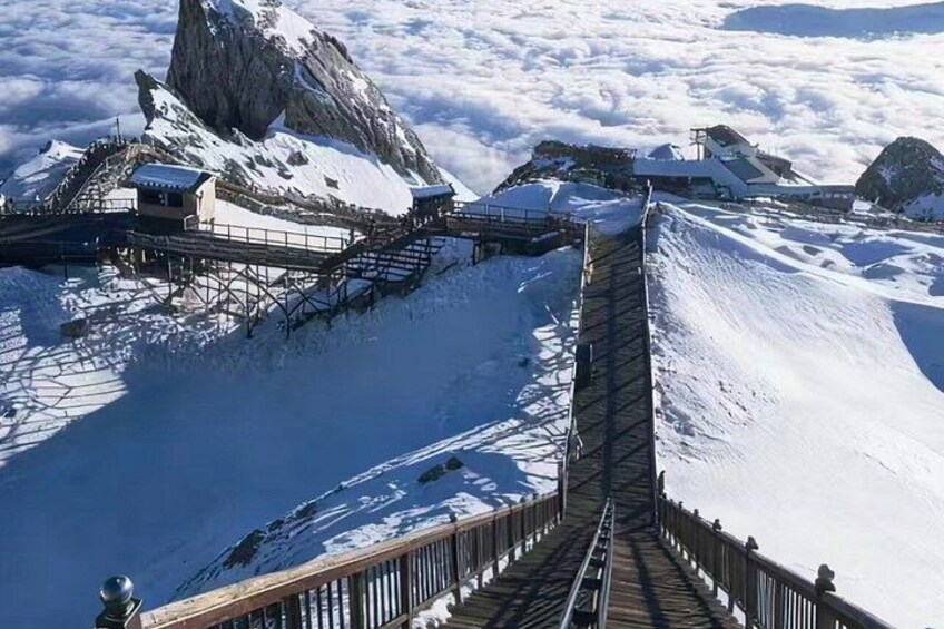 A snow-covered mountain with a wooden bridge leading to a building. 4