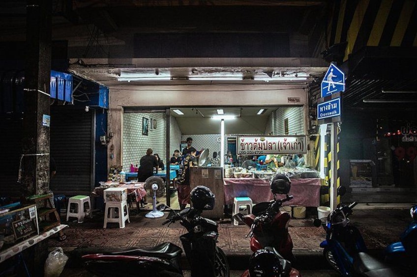 A street food stall at night with a blue sign, motorcycles parked in front, and a person standing near the entrance. 5