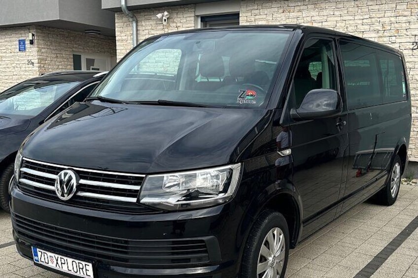Een zwarte Volkswagen bestelwagen geparkeerd voor een gebouw met een bakstenen gevel. 2