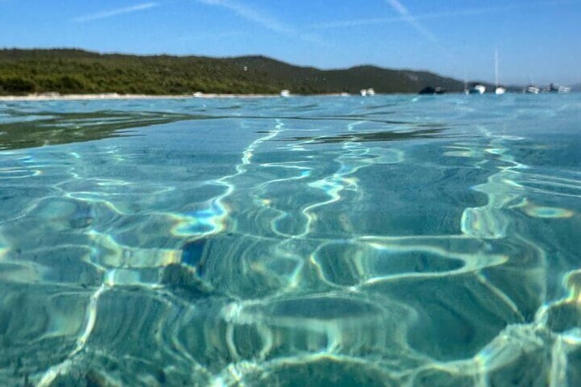 Helder water met zichtbare zandpatronen en verre boten aan het strand. 4