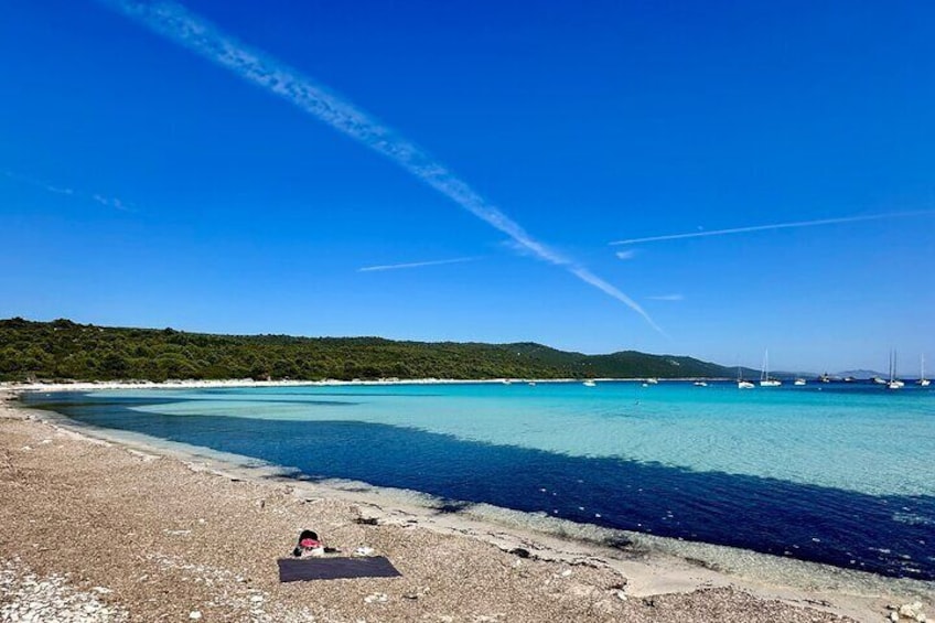 Een strand met helder turquoise water, een zandstrand en zeilboten in de verte. 5