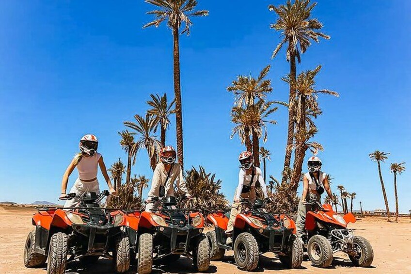Quatre personnes sur des quads, dans un désert parsemé de palmiers. 1