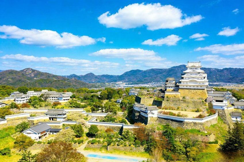 Un castillo japonés tradicional con varios niveles, rodeado de exuberante vegetación y un cielo azul despejado. 2