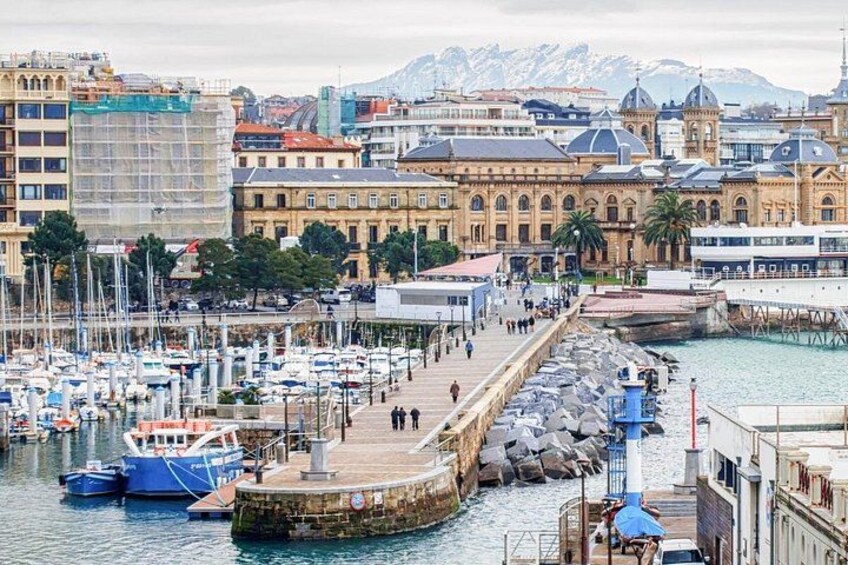 En hamn med båtar, en brygga och byggnader, med berg i bakgrunden. 5
