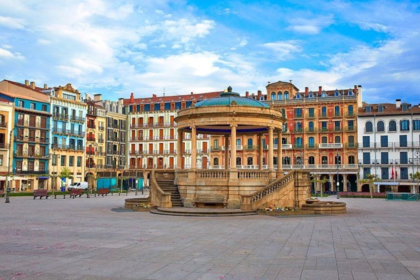 A historic plaza with a central fountain, surrounded by colorful buildings. 3