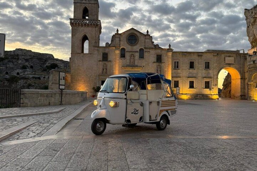 A vintage car parked in front of a historic building with a bell tower. 4