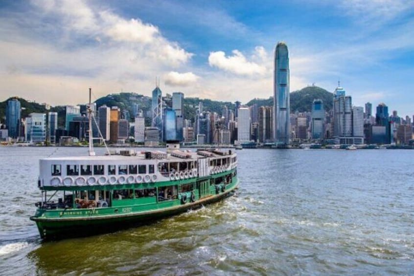 A green and white boat with multiple decks sailing on water, with a city skyline in the background. 5