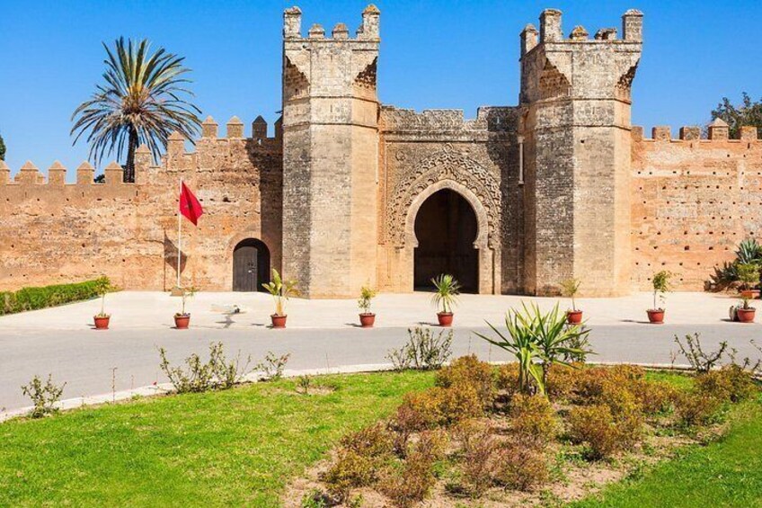 Una histórica puerta de piedra con arcos de entrada, una bandera roja y plantas en macetas en un área ajardinada. 4
