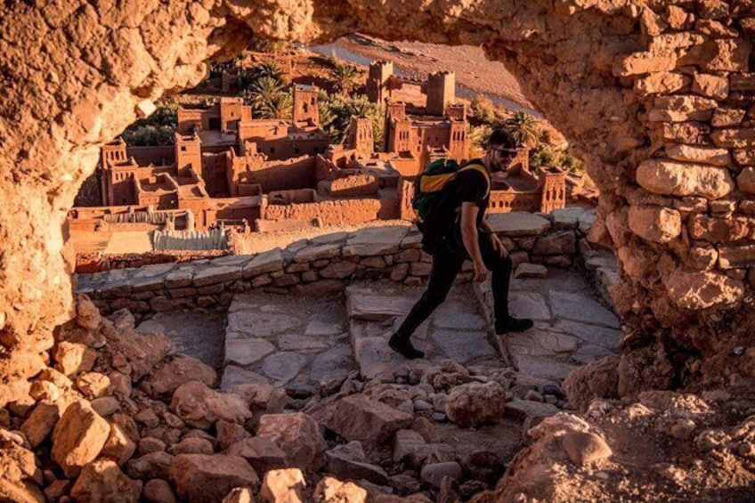 A person walking through a stone archway overlooking a historic village with traditional architecture. 1