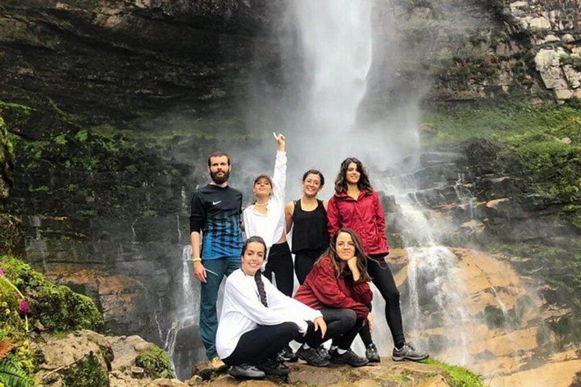 Een groep mensen poseert voor een waterval, met opwaartse mist uit het water. 4