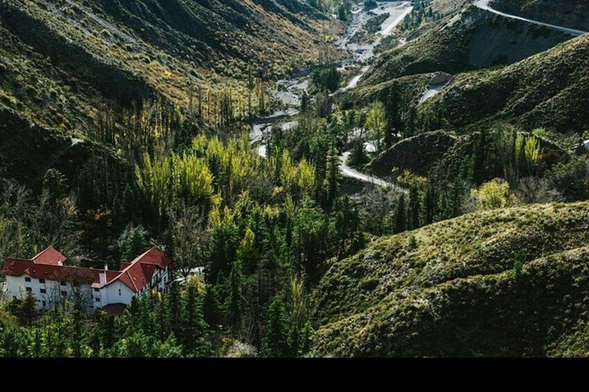 Een bergachtig landschap met een kronkelende weg, een gebouw met een rood dak en dicht bos. 5