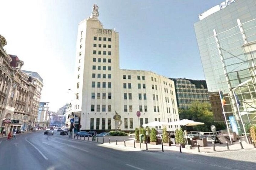 Une rue de la ville avec un imposant bâtiment blanc surmonté d’une tour, un bâtiment moderne en verre et un ciel dégagé. 2