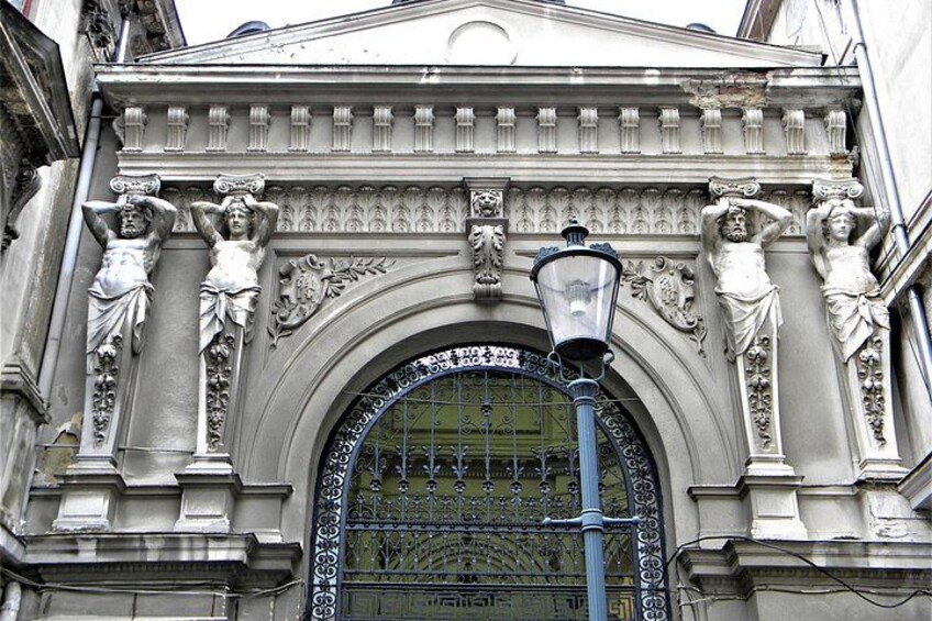 Une façade de style classique, ornée de sculptures, avec une grande entrée en arc de cercle et un lampadaire. 5