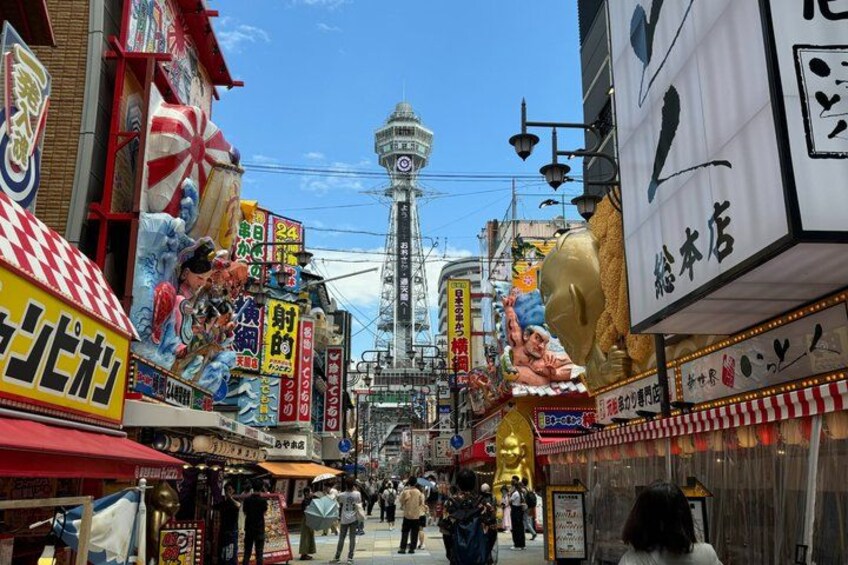 Una calle concurrida con diversas tiendas y una torre destacada al fondo. 5