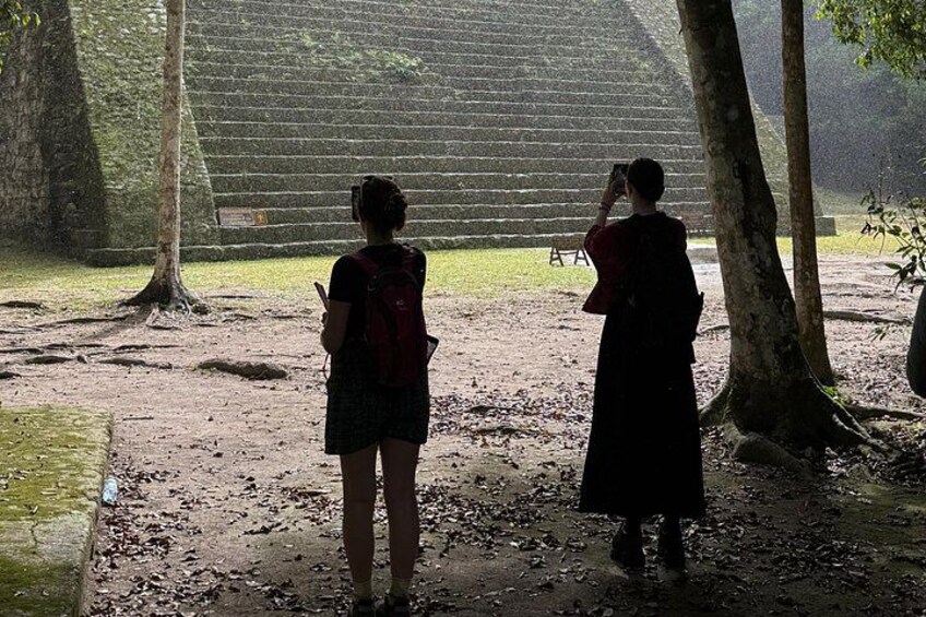 Two people taking photographs of a stone structure in a forested area. 5
