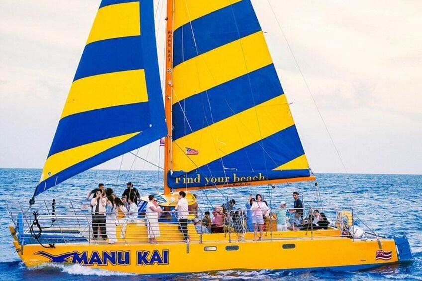 A yellow and blue sailboat named MANU KAI with passengers on board. 2