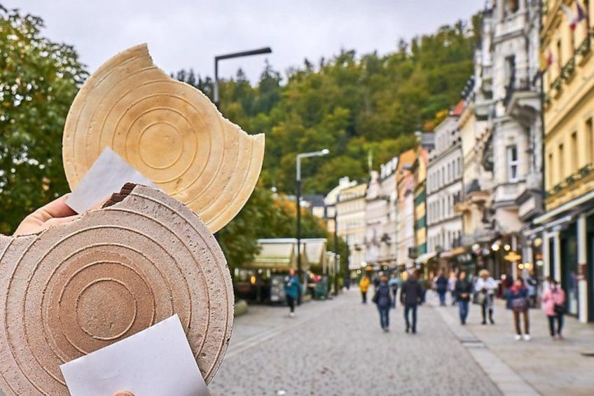 A cobblestone street with historic buildings, a person holding a wooden object, and a crowd in the background. 5