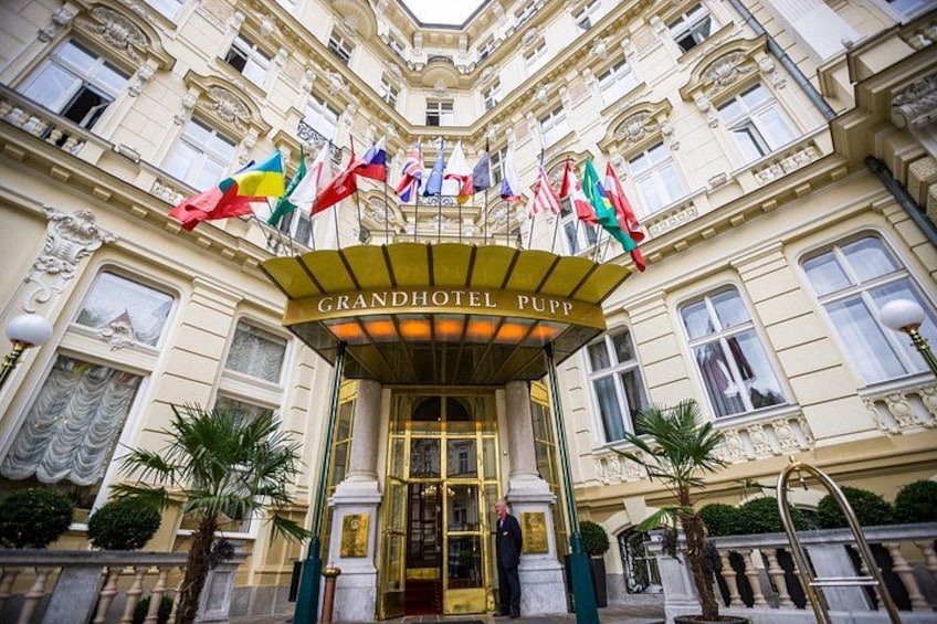 The Grandhotel Pupp entrance with flags, a golden entrance canopy, and classical architecture. 4