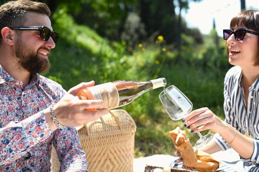 Deux personnes trinquent avec des coupes de champagne à l’extérieur, entourées de verdure. 1