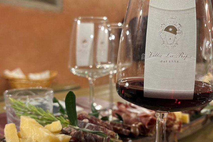 Una botella de vino con etiqueta, una copa de vino tinto y una tabla de embutidos y quesos variados. 3