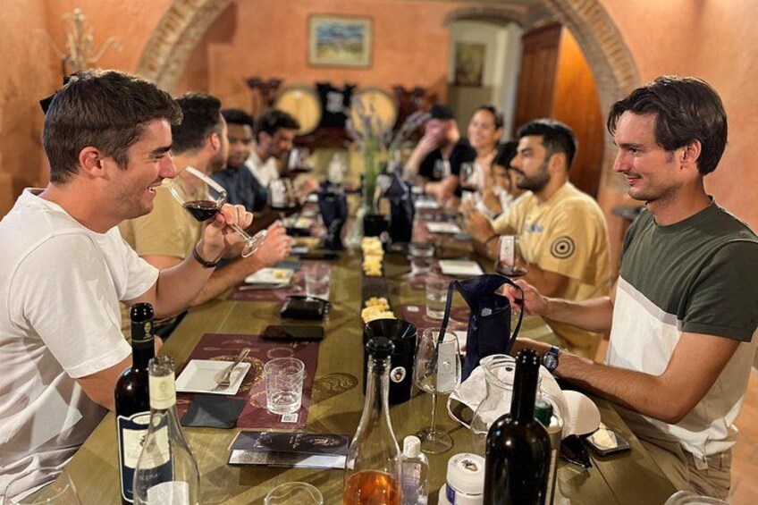 Un grupo de personas sentadas a una larga mesa en una sala con arcos, participando en una cata de vinos. 2