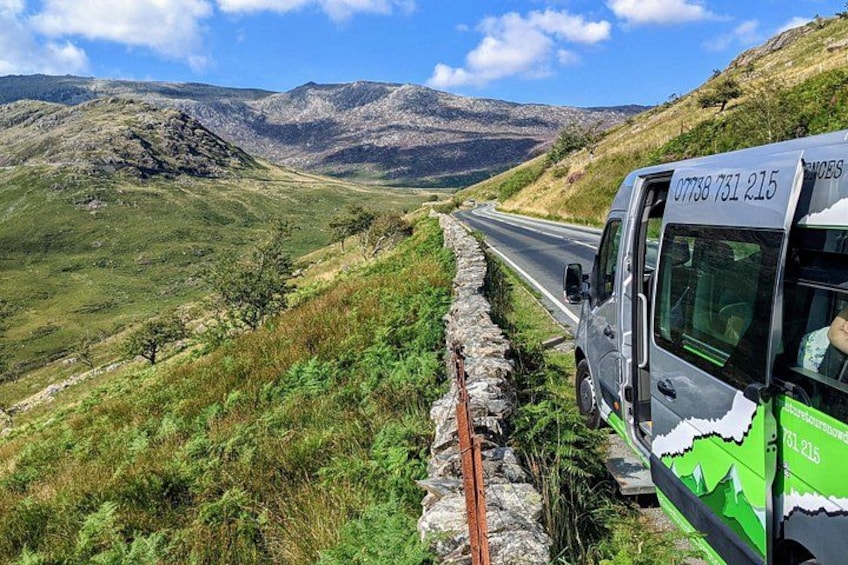 Une route bordée d’un mur de pierres, un autobus vert et un paysage montagneux. 3