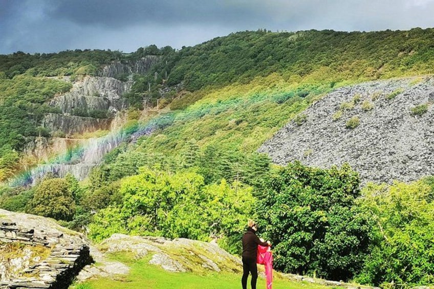 Une personne se tient sur une colline herbeuse, avec un arc-en-ciel en arrière-plan. 5