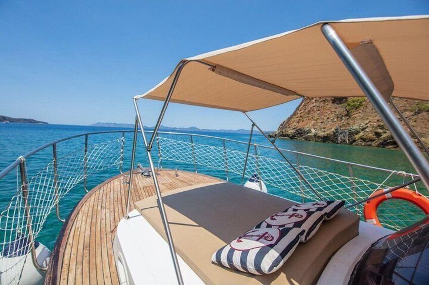 A boat deck with a cushioned seat, a life ring, and a clear view of the sea and coastline. 4