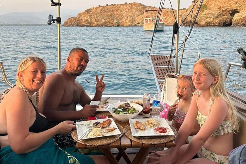 En grupp människor som äter middag på en båt med en klippig kustlinje i bakgrunden. 4