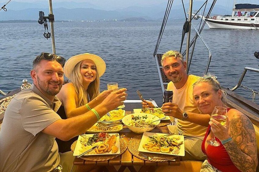 A group of people dining on a boat with a body of water and distant mountains in the background. 2