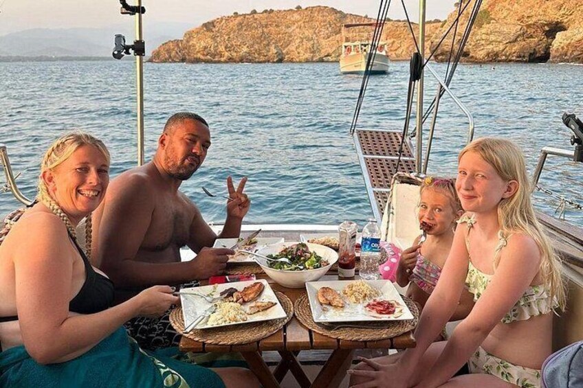 Une famille prend son repas sur un bateau, avec une côte rocheuse en arrière-plan. 5