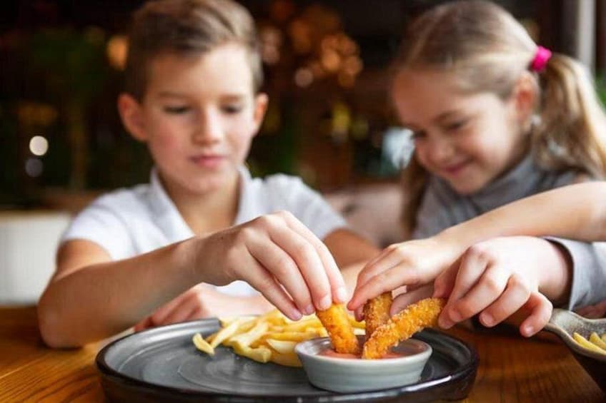 Dos niños mojando tiras de pollo frito en un tazón de salsa. 3