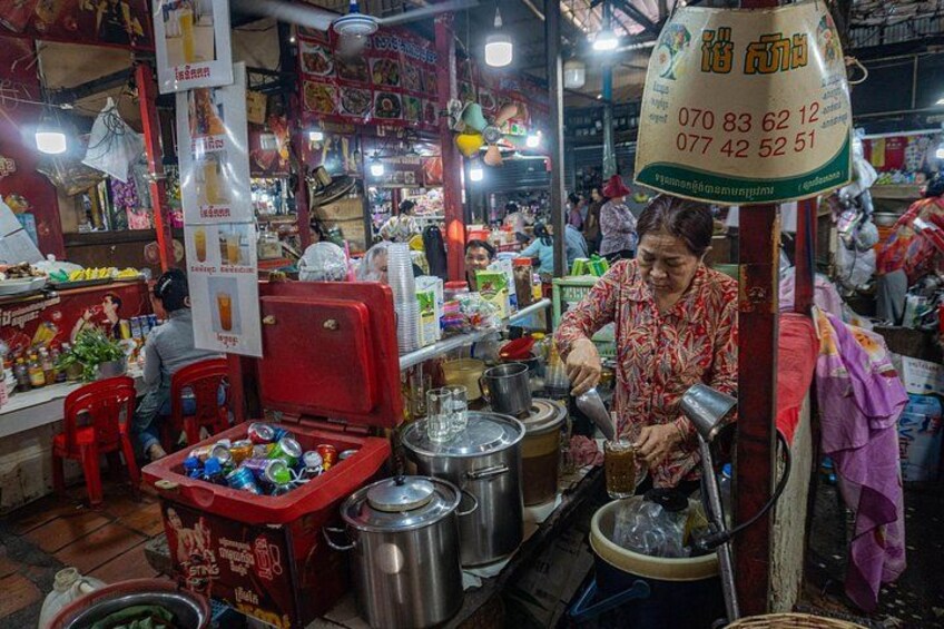 Un marché animé où l'on trouve des stands de nourriture de rue, des vendeurs préparant des plats, une grande variété de produits et un panneau indiquant les numéros de téléphone à contacter. 2