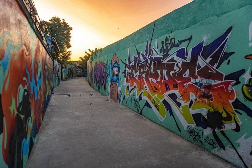 A graffiti-covered alleyway with a concrete floor and a sunset in the background. 4